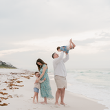 Family of four on a beach with a man lifting a child