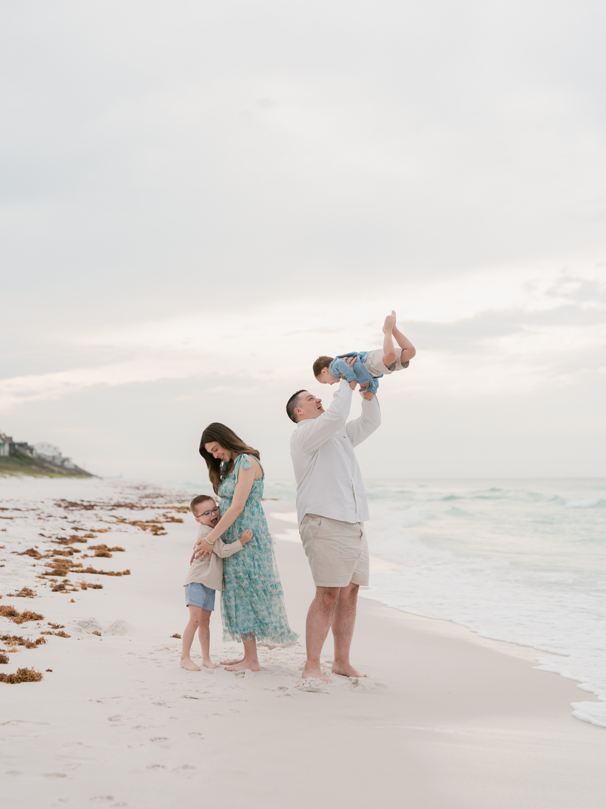 Family of four on a beach with a man lifting a child
